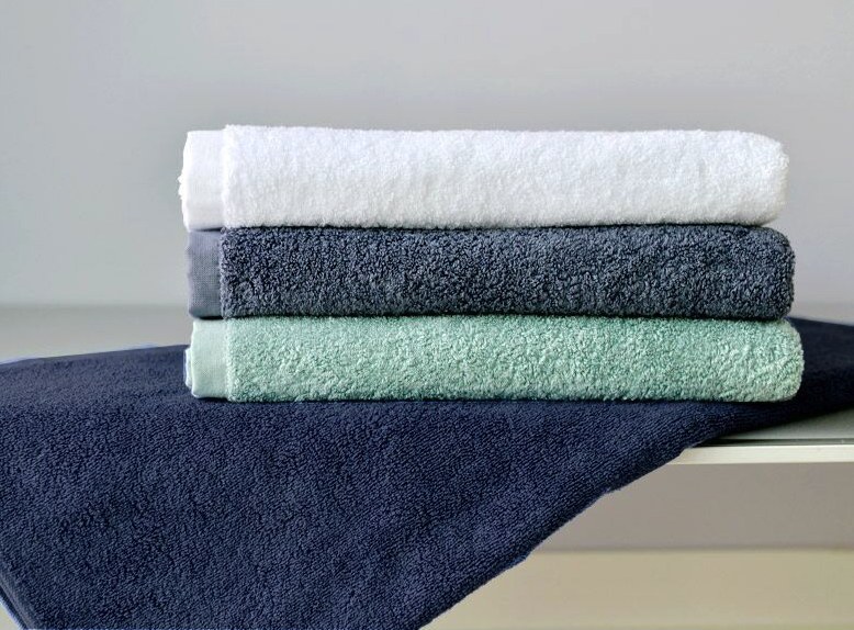 Folded bath towels in white, gray and mint on a navy towel